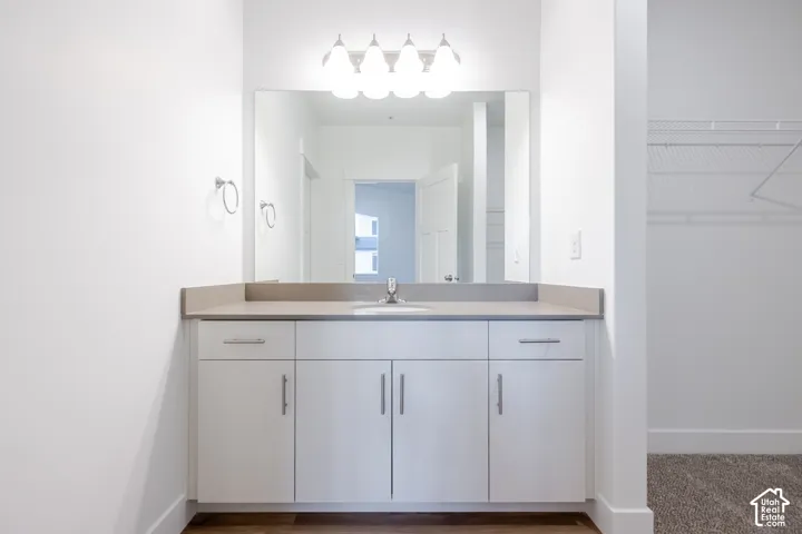 Vanity featuring white cabinetry, a neutral-toned countertop, integrated basin, chrome fixtures, and a wall-mounted light fixture above a large mirror