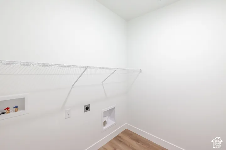 Utility area featuring wood-finish flooring, white walls, built-in wire shelving, and dedicated water and dryer hookups
