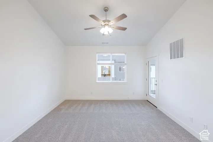 Vaulted ceilings, neutral carpeting, a central multi-blade ceiling fan with integrated lighting, a single-pane window, and an exterior glass-panel door