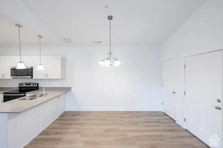 Open floor plan featuring wood-finish flooring, white cabinetry, solid-surface countertops, and decorative pendant lighting