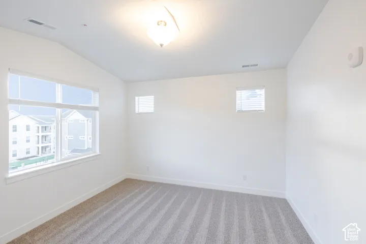 Vaulted ceilings, neutral carpeting, large picture window, and recessed accent windows