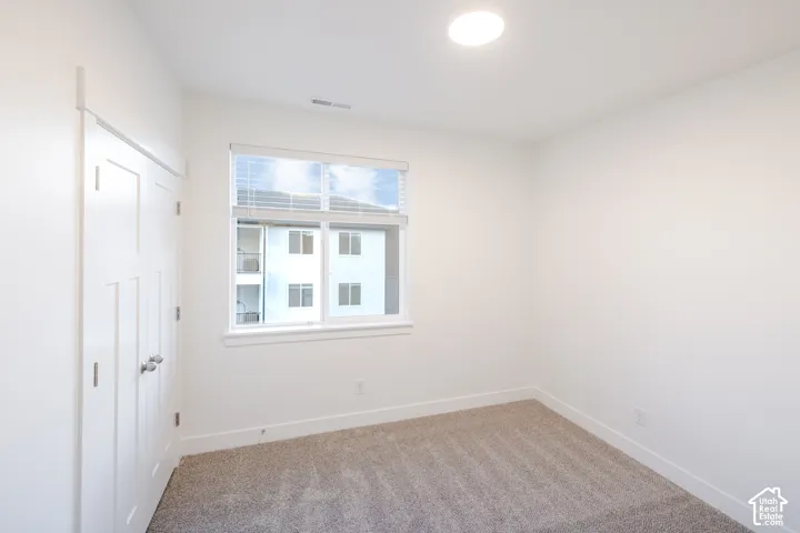 Neutral-toned carpeting, white walls, dual-pane window with installed blinds, and closet with double doors