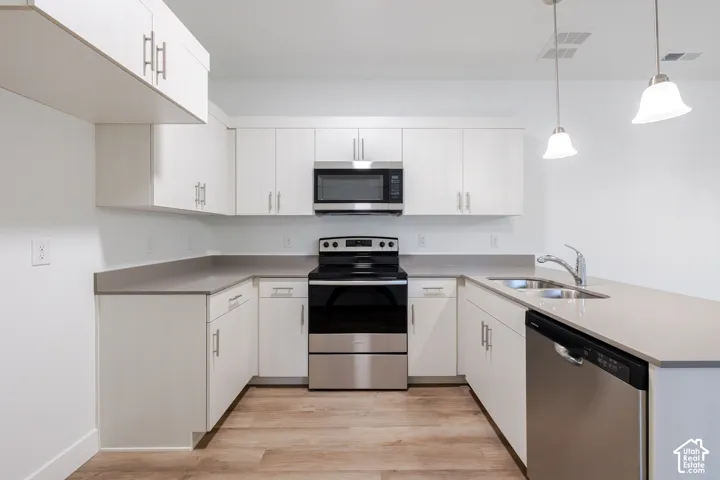 Kitchen featuring white cabinetry, solid-surface countertops, stainless steel appliances, dual pendant lighting, and wood-finish flooring