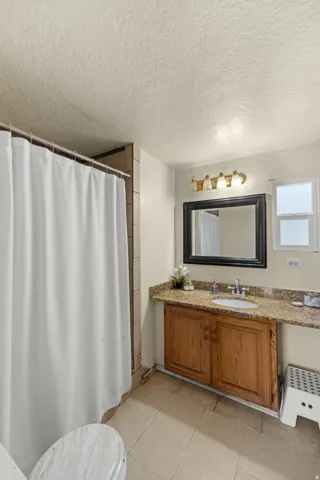 Full bath with vanity, a shower with curtain, a textured ceiling, and light tile patterned floors