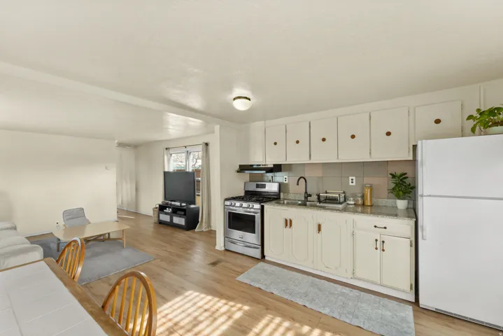Kitchen with freestanding refrigerator, stainless steel range with gas cooktop, light wood-style floors, and white cabinetry