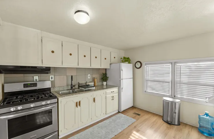 Kitchen with stainless steel range with gas stovetop, freestanding refrigerator, decorative backsplash, light countertops, and light wood-style floors