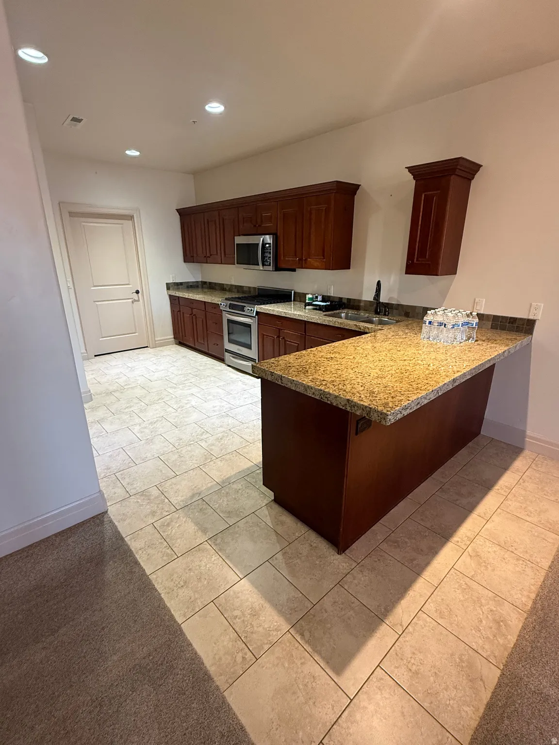 Kitchen with a peninsula, stainless steel appliances, light stone countertops, a kitchen bar, and recessed lighting
