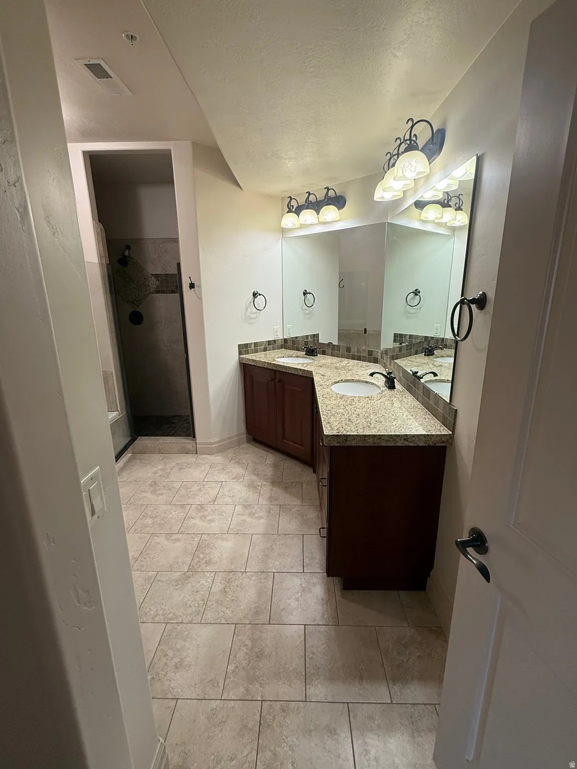 Full bathroom featuring double vanity, a stall shower, a textured ceiling, and light tile patterned floors
