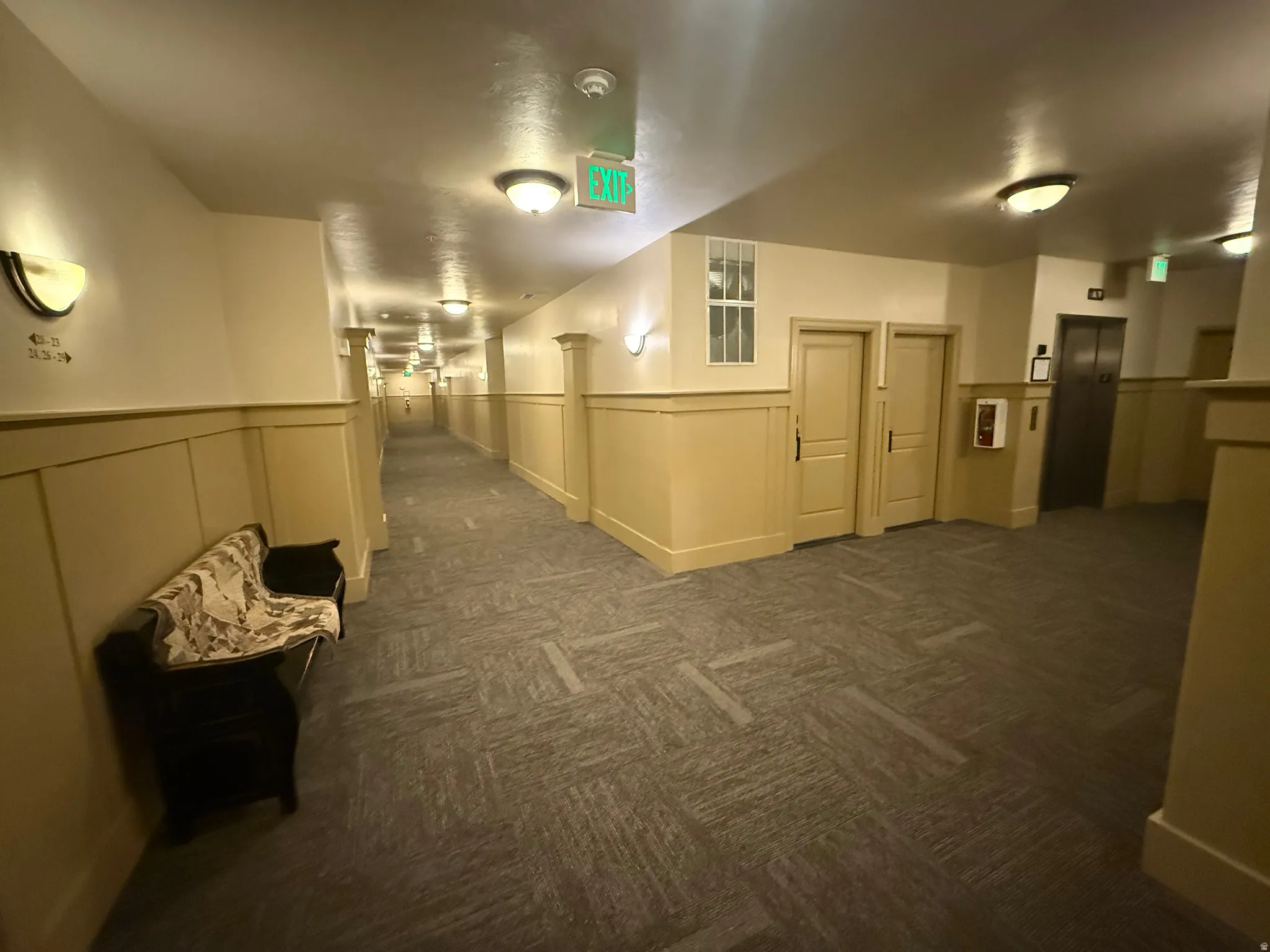 Hall with elevator, wainscoting, dark colored carpet, and a decorative wall