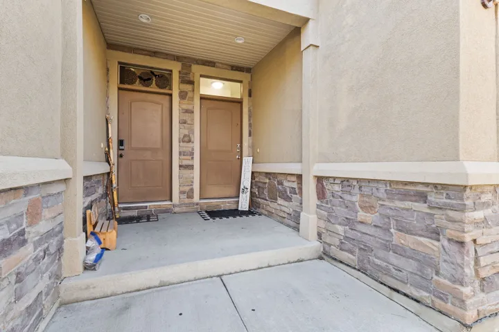 View of exterior entry featuring stone siding, stucco siding, and covered porch