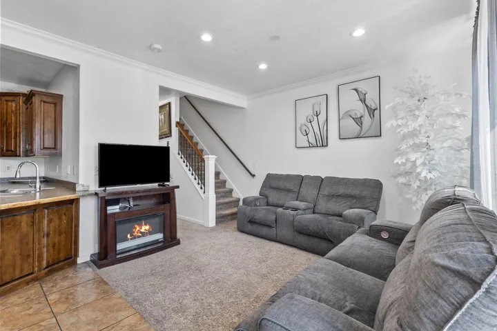 Living area with ornamental molding, a glass covered fireplace, recessed lighting, light tile patterned flooring, and light colored carpet