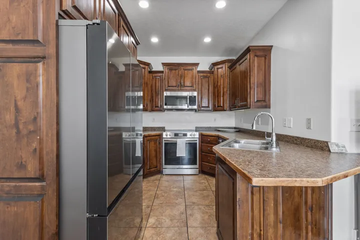 Kitchen with stainless steel appliances, dark countertops, dark wood finish cabinetry, recessed lighting, and light tile patterned flooring