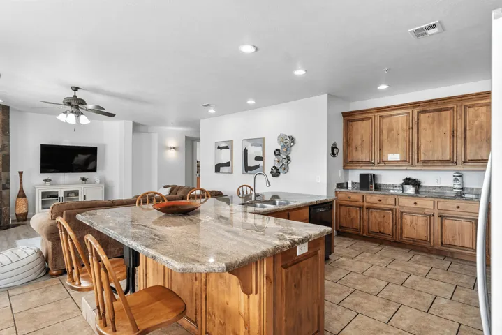 Kitchen featuring wood finish cabinetry, open floor plan, an island with sink, a kitchen breakfast bar, and light stone counters