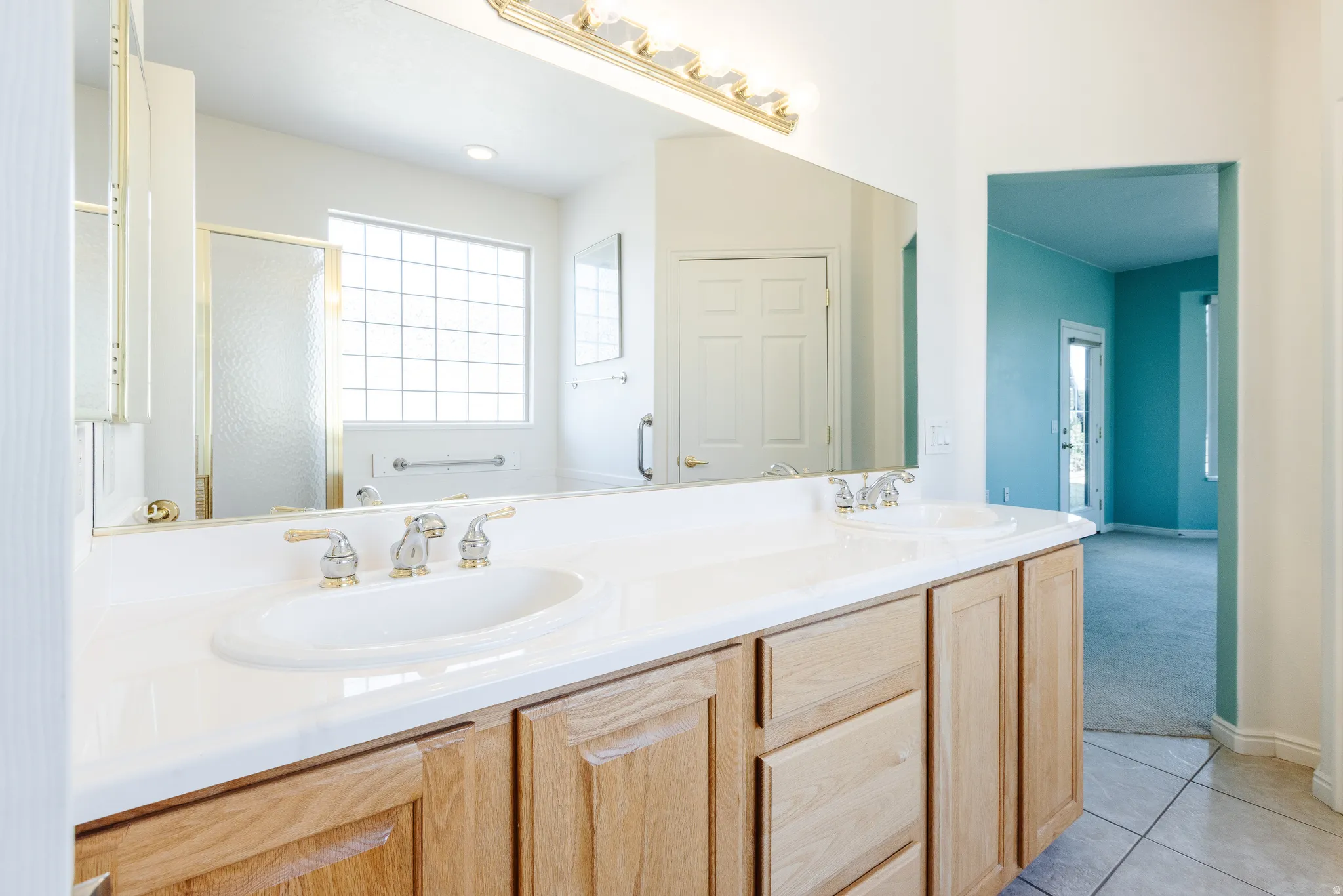 Full bathroom featuring double vanity, a stall shower, light tile patterned floors, and light colored carpet
