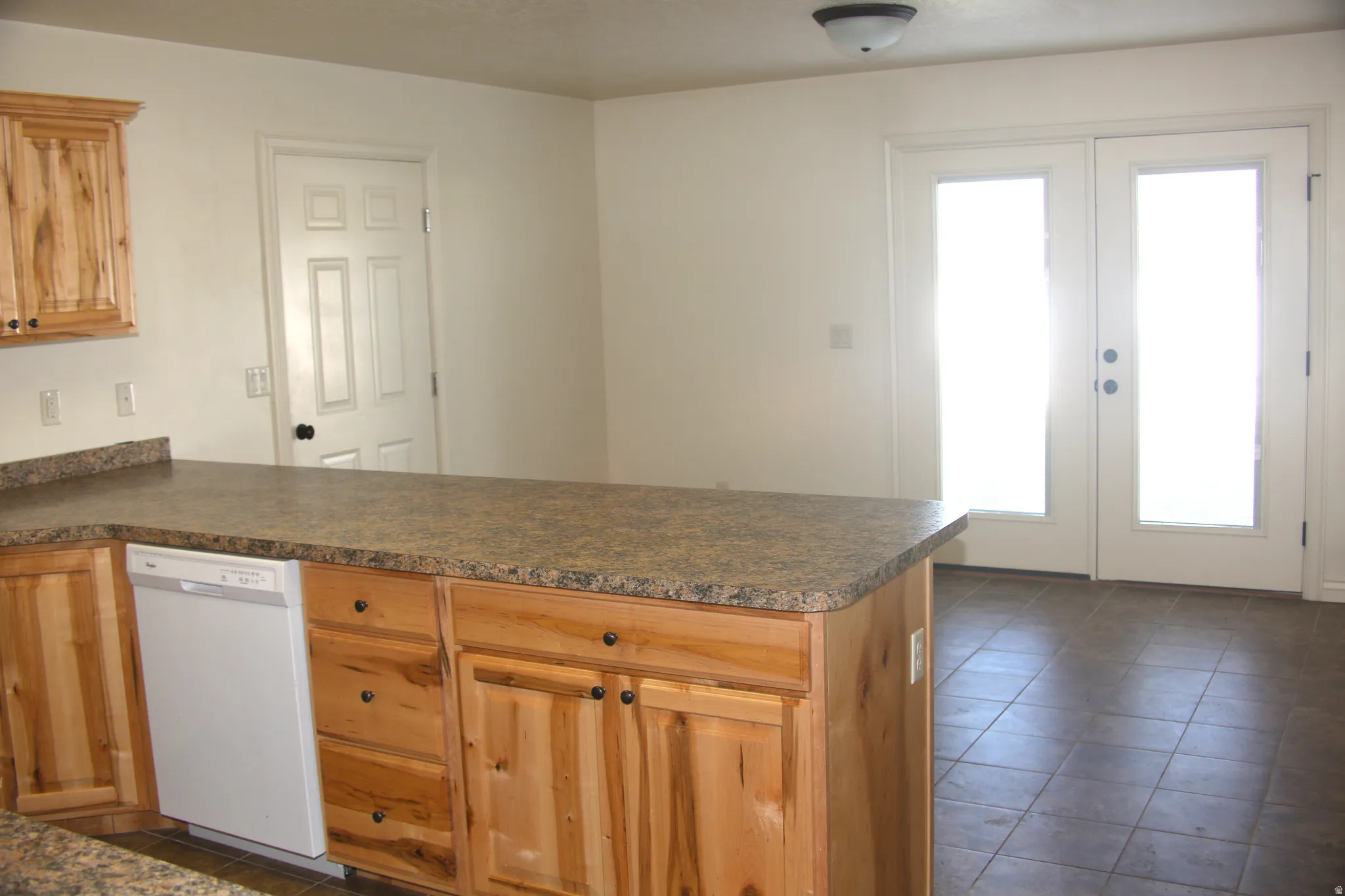 Kitchen with french doors, dark countertops, dishwasher, a peninsula, and dark tile patterned flooring