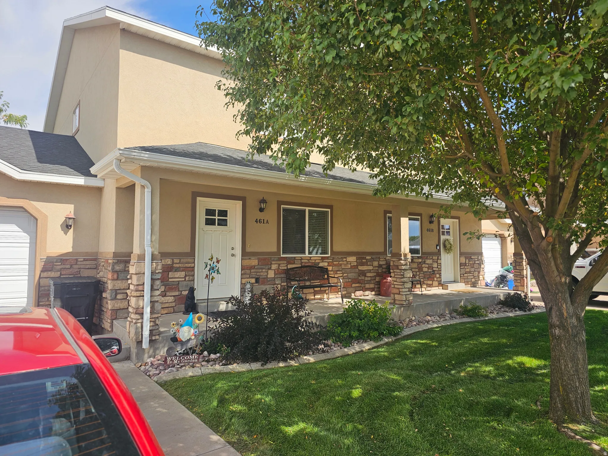 View of front facade with covered porch, stucco siding, a front yard, stone siding, and a garage