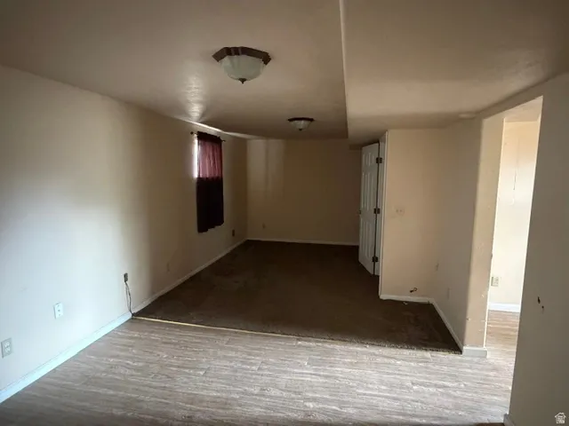 Spacious room featuring neutral wall tones, two distinct flooring types, and a window with existing window treatments
