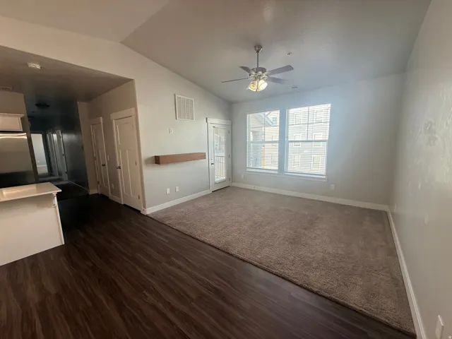 Unfurnished living room featuring ceiling fan, vaulted ceiling, and dark wood-style floors