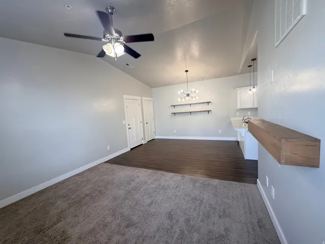 Unfurnished living room featuring a chandelier, lofted ceiling, dark colored carpet, and ceiling fan