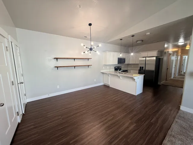 Kitchen with white cabinets, stainless steel appliances, lofted ceiling, dark wood-style floors, and a peninsula