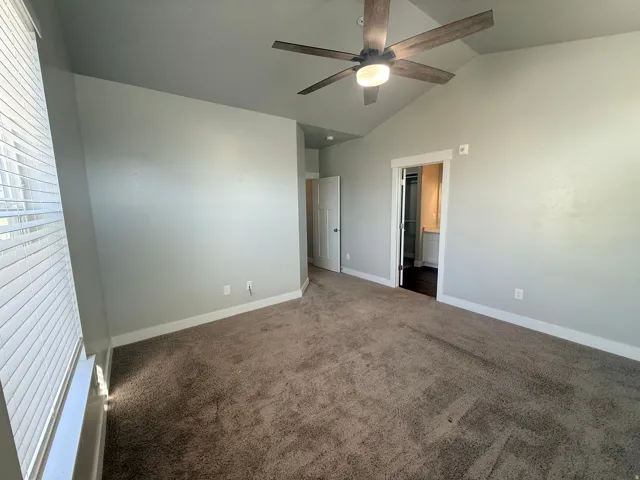 Unfurnished bedroom featuring vaulted ceiling, carpet floors, a ceiling fan, and ensuite bathroom
