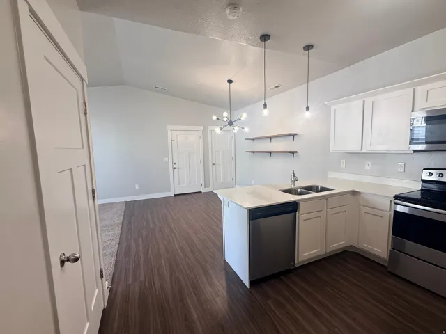 Kitchen with a peninsula, stainless steel appliances, white cabinetry, suspended lighting, and lofted ceiling