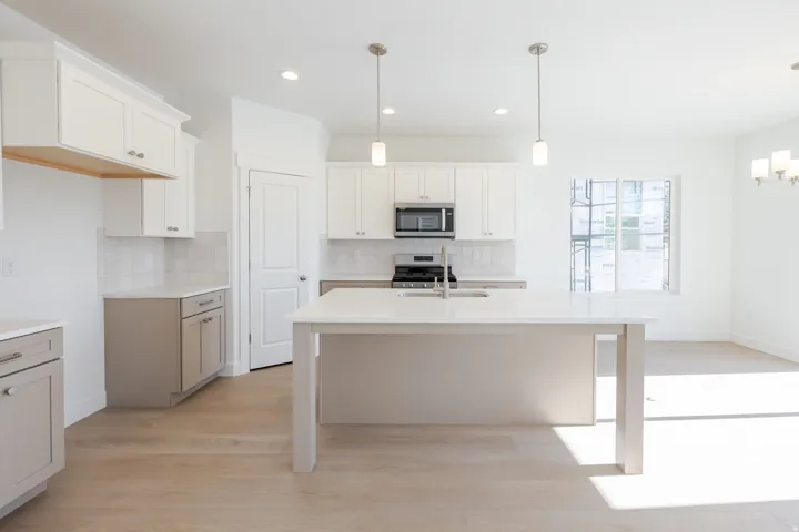 Modern kitchen featuring light wood-finish flooring, a central island with a white countertop, two-tone cabinetry, stainless steel appliances, and a tiled backsplash