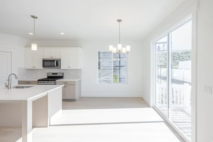 Bright open-concept kitchen and dining area featuring light wood-finish flooring, white cabinetry, stainless steel appliances, a kitchen island with sink, and a large sliding glass door