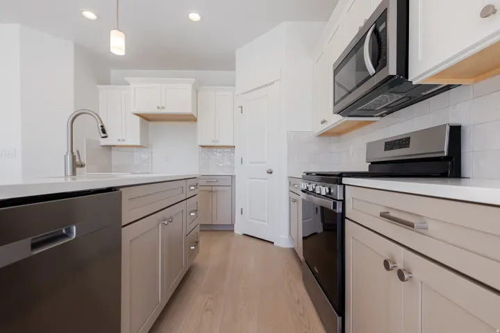 Kitchen featuring white upper cabinetry, gray lower cabinetry, stainless steel appliances, a tile backsplash, and wood-finish flooring