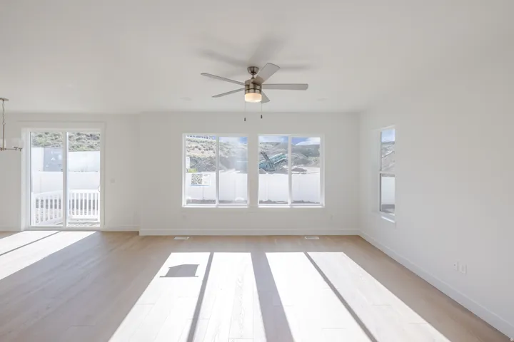 Bright living area featuring wood-finish flooring, white walls, and a ceiling fan with integrated lighting