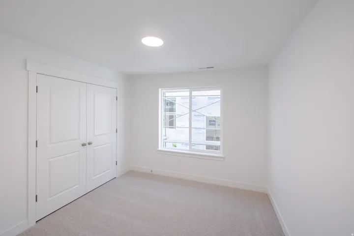 Neutral-toned carpeting extends throughout this room, featuring a double-door closet with paneling and brushed nickel hardware
