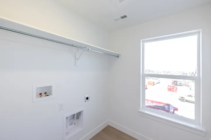 Dedicated utility space featuring a window, built-in shelving, a clothing rod, and wood-finish flooring
