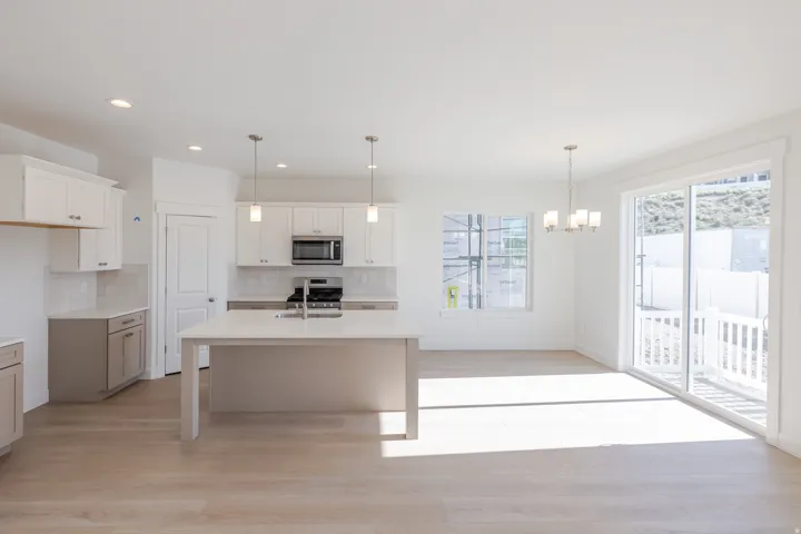 Kitchen and dining area featuring a central island with sink, stainless steel appliances, wood-finish flooring, white cabinetry, and a sliding glass door leading to a patio