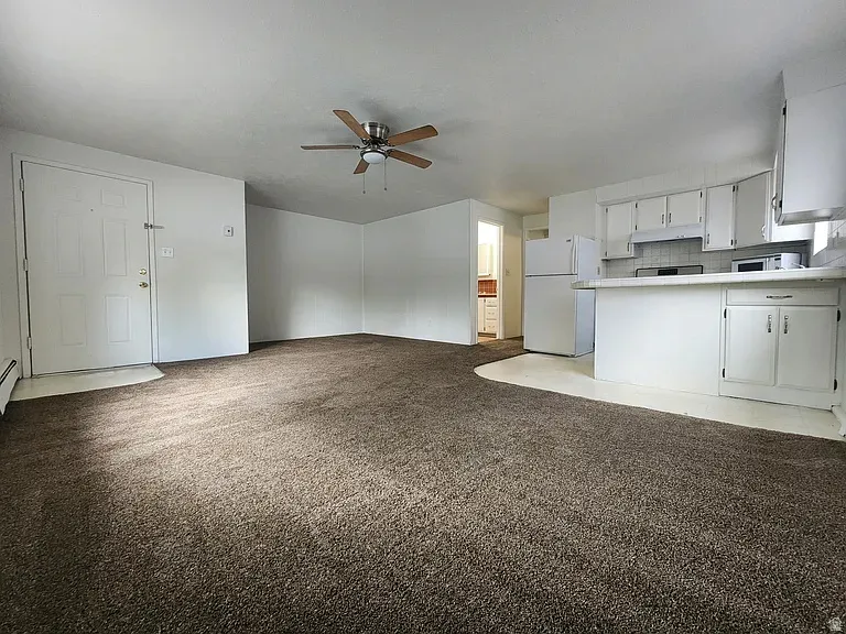 Kitchen featuring open floor plan, freestanding refrigerator, a ceiling fan, light countertops, and white cabinets