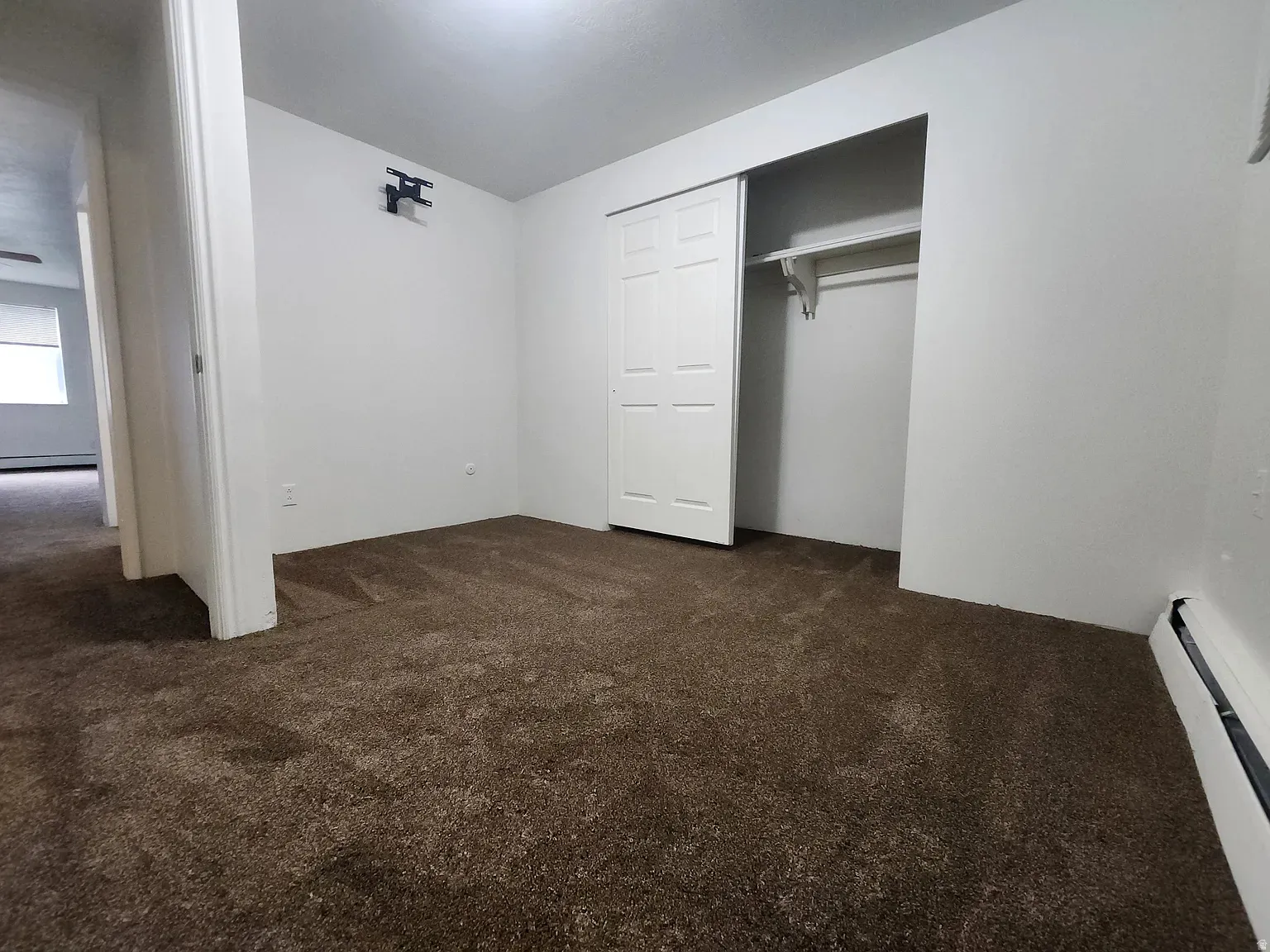 Unfurnished bedroom featuring dark colored carpet, baseboard heating, and a closet