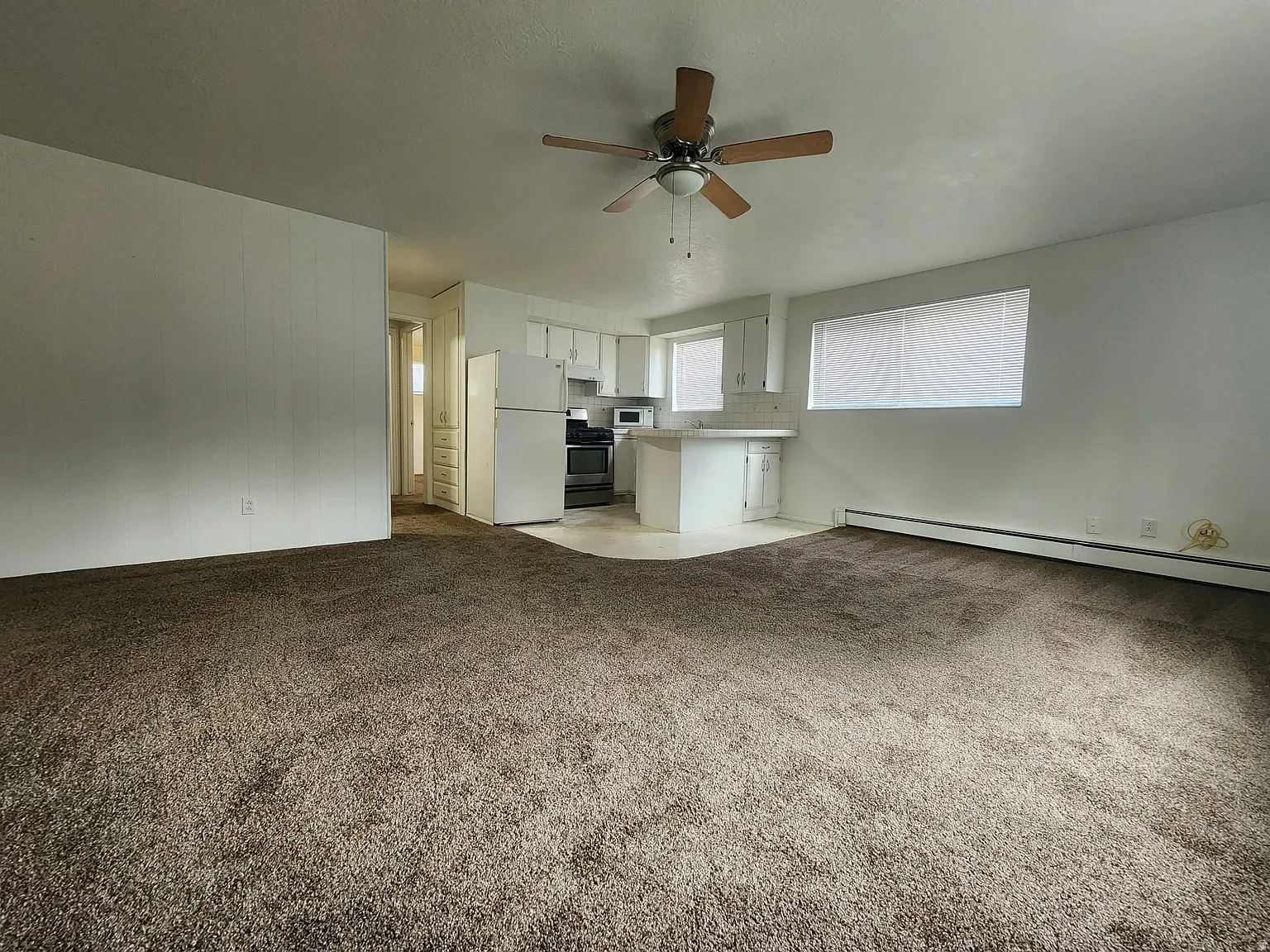 Unfurnished living room with ceiling fan, light carpet, and a baseboard heating unit