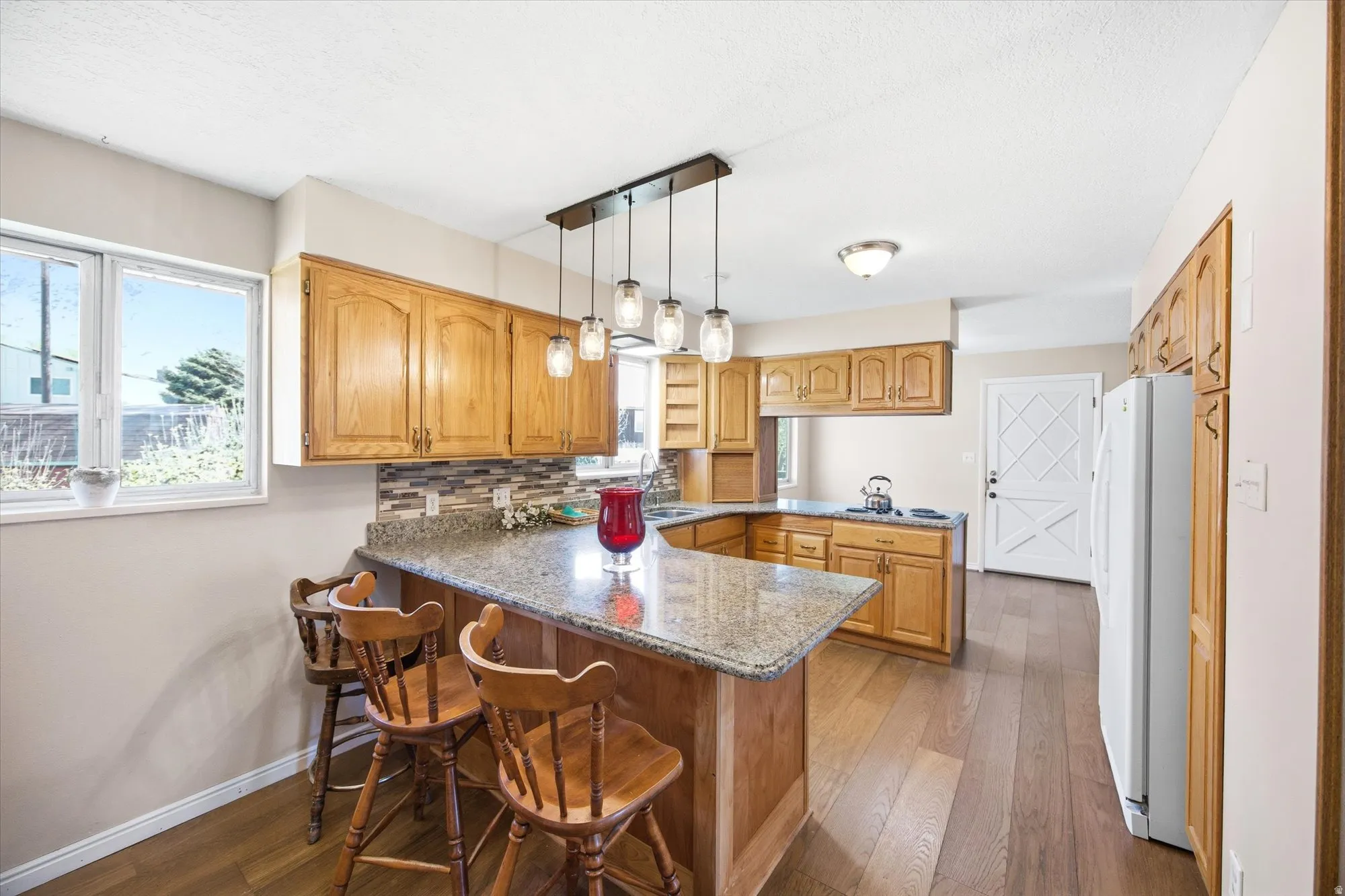 Kitchen with a peninsula, freestanding refrigerator, light wood finished floors, light stone countertops, and backsplash