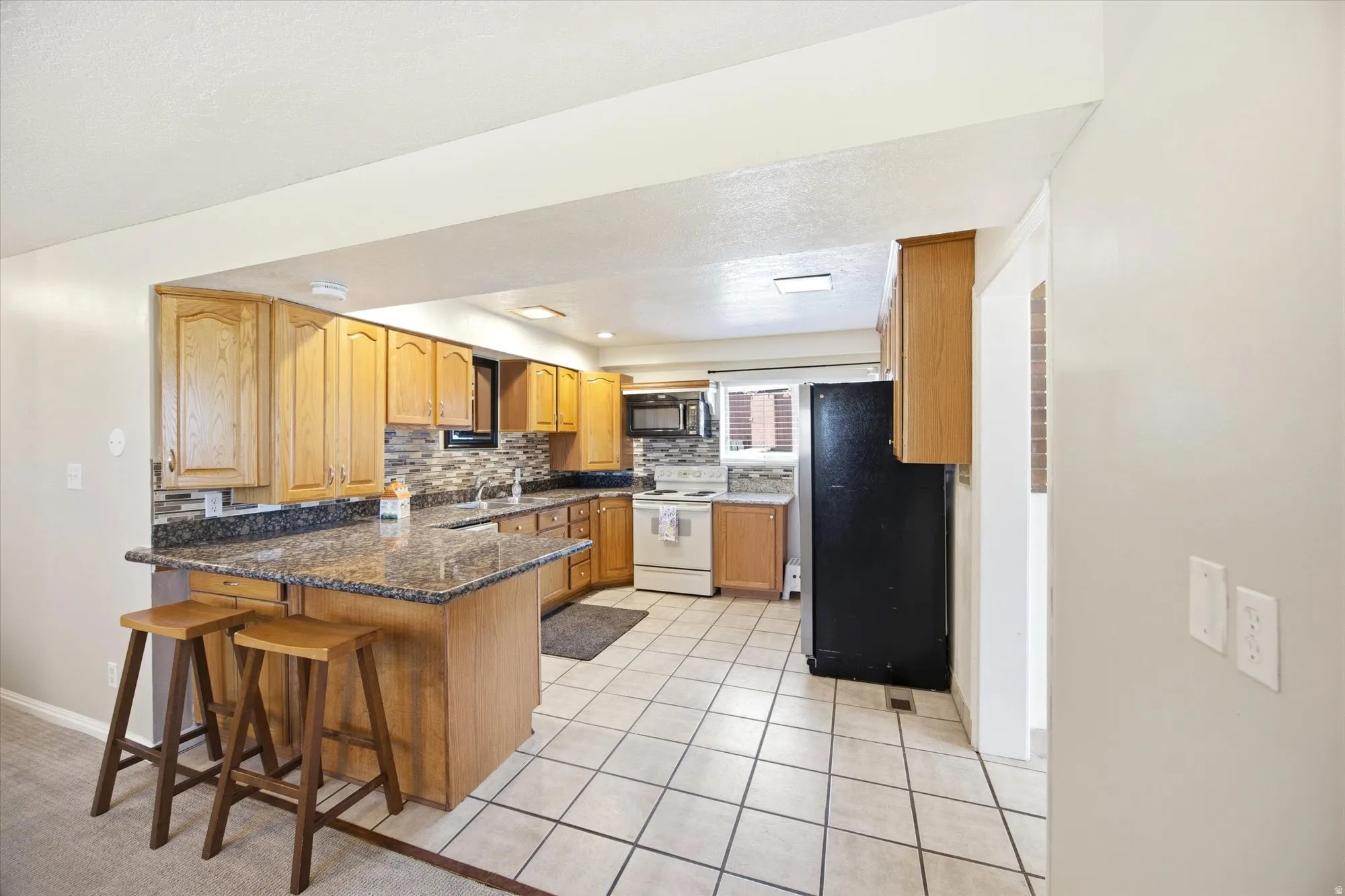 Kitchen with black appliances, a peninsula, a breakfast bar, light tile patterned floors, and backsplash