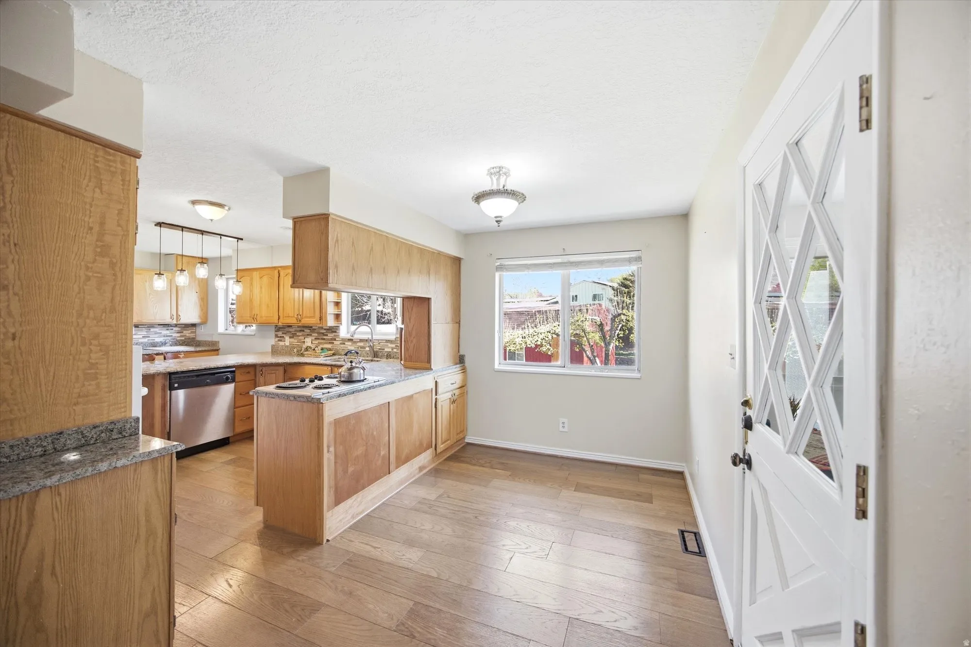 Kitchen with a peninsula, light wood-style flooring, dishwasher, healthy amount of natural light, and a textured ceiling