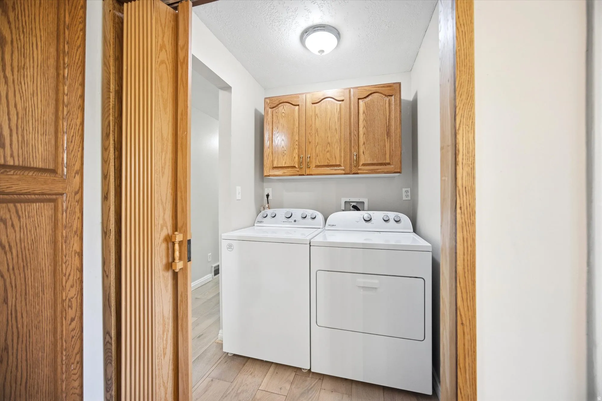 Laundry area featuring light wood-style floors, a textured ceiling, cabinet space, and washing machine and dryer