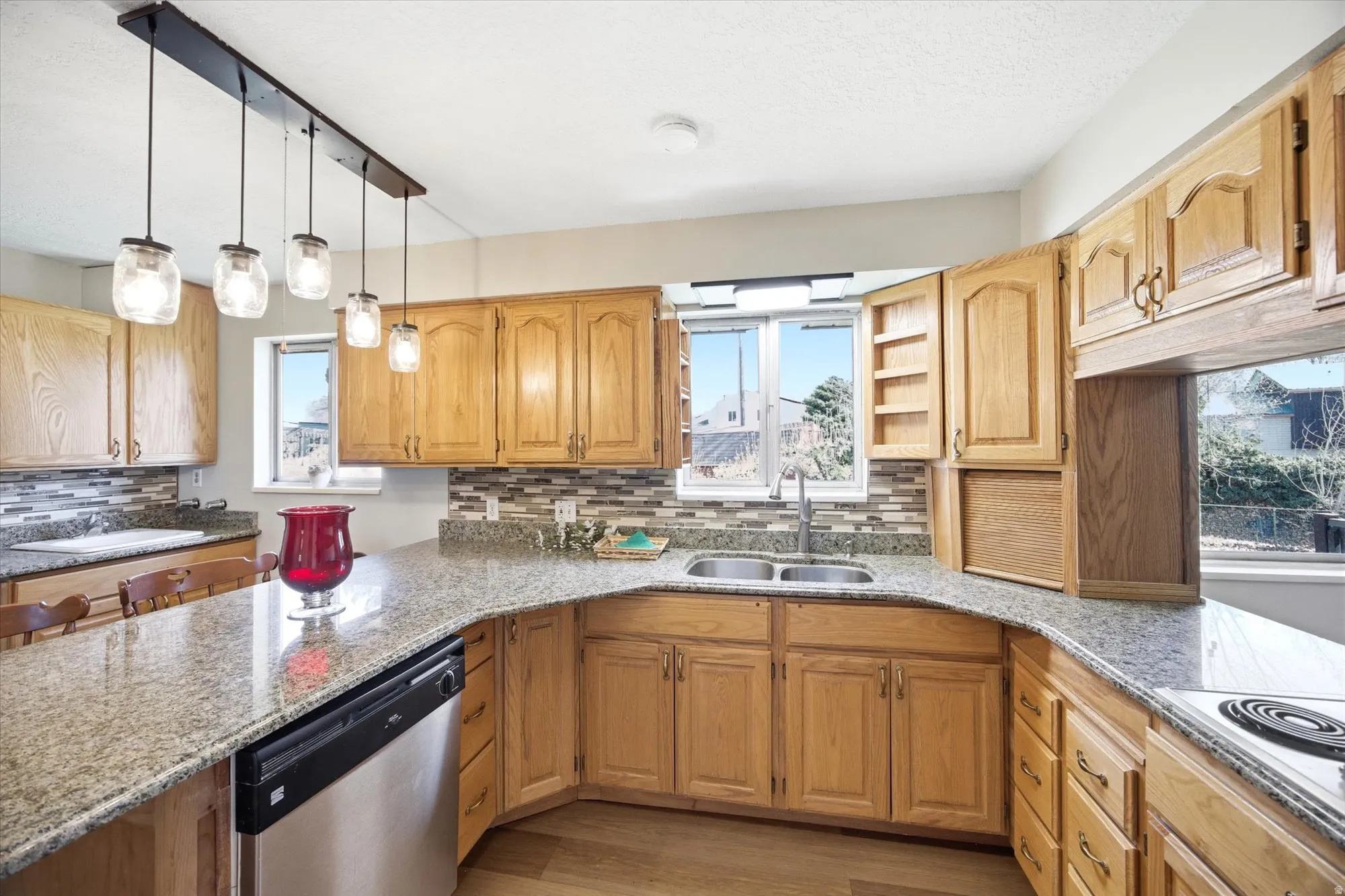 Kitchen featuring stainless steel dishwasher, decorative backsplash, light stone counters, electric cooktop, and light wood-style flooring