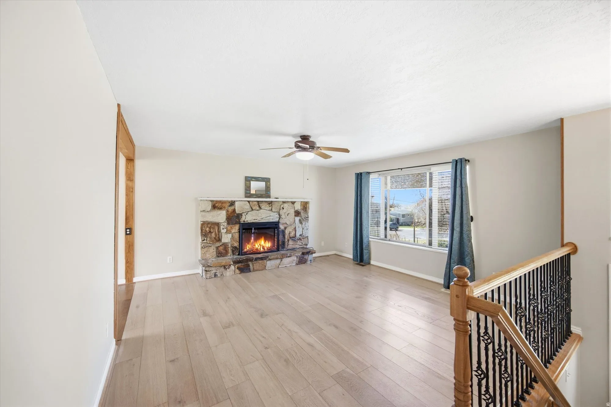 Living room with light wood-type flooring, ceiling fan, and a stone fireplace