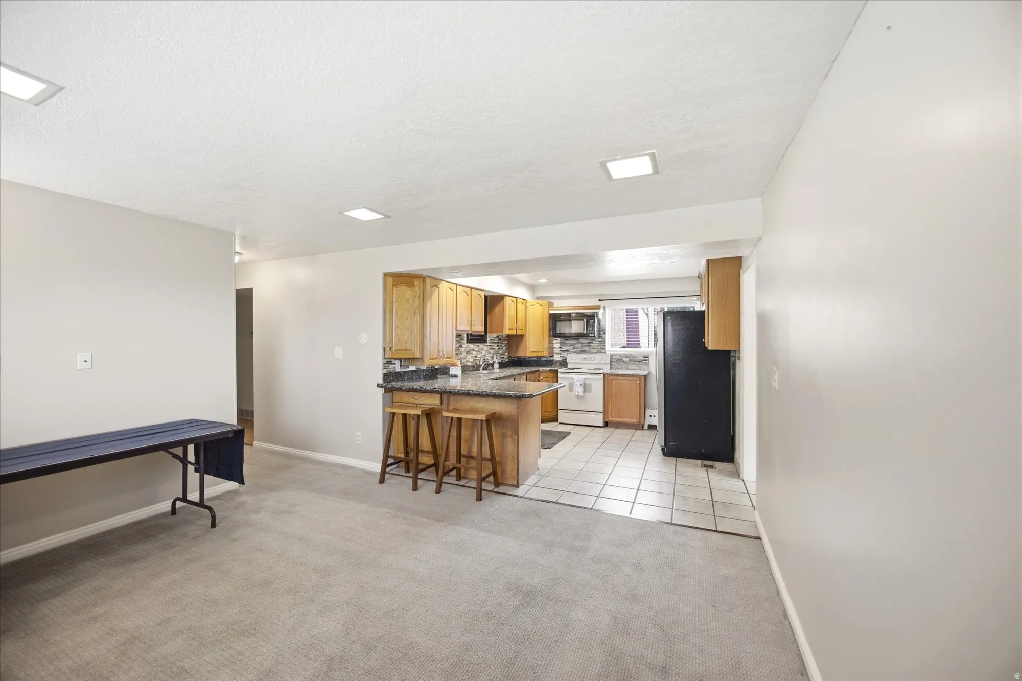 Kitchen featuring a peninsula, tasteful backsplash, freestanding refrigerator, a kitchen bar, and light colored carpet