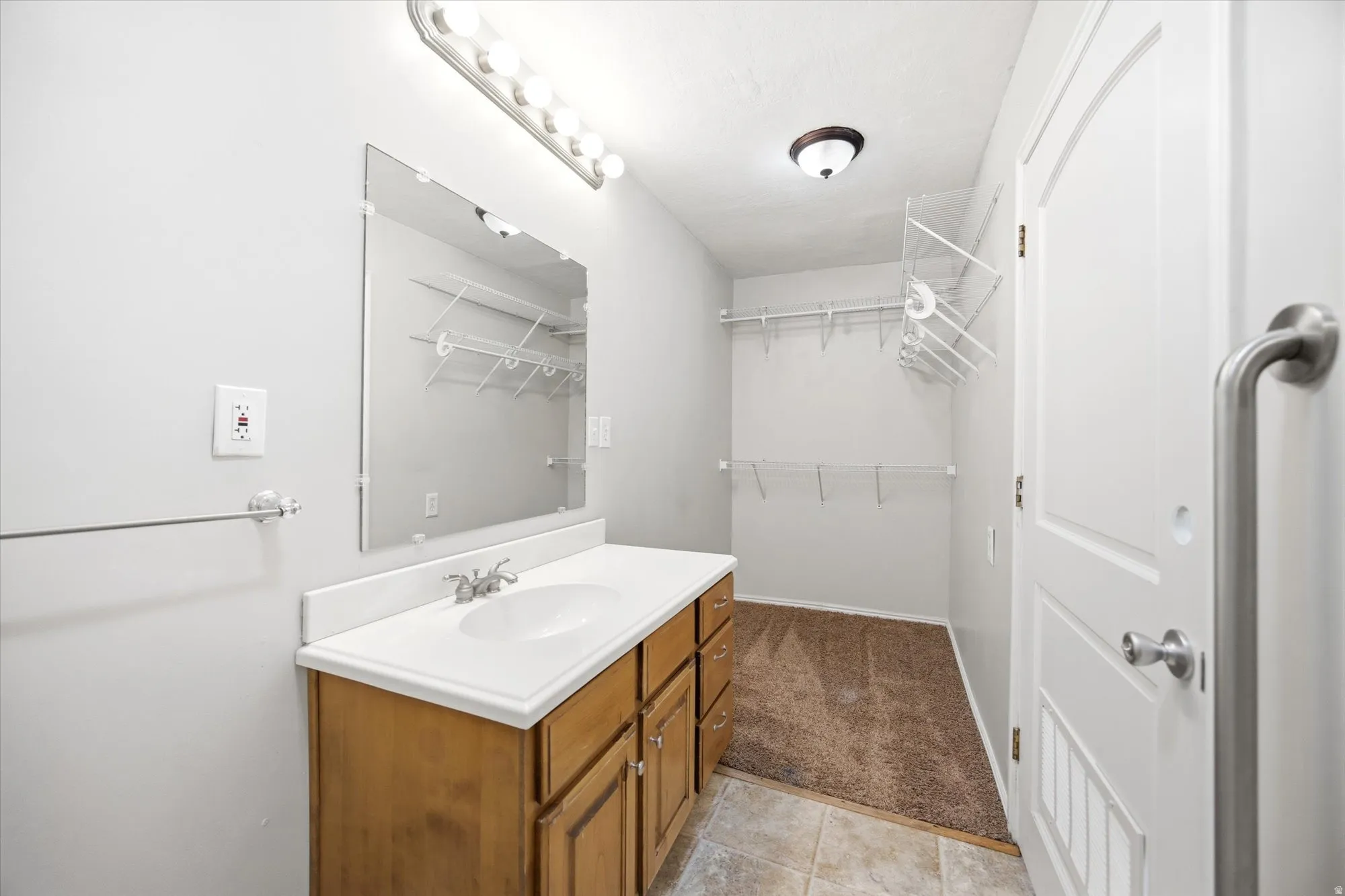 Bathroom featuring vanity, a spacious closet, light carpet, and light tile patterned floors