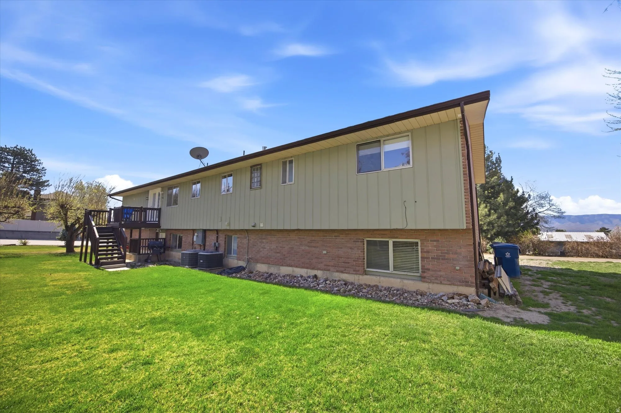 Rear view of house featuring a deck, a lawn, brick siding, and board and batten siding