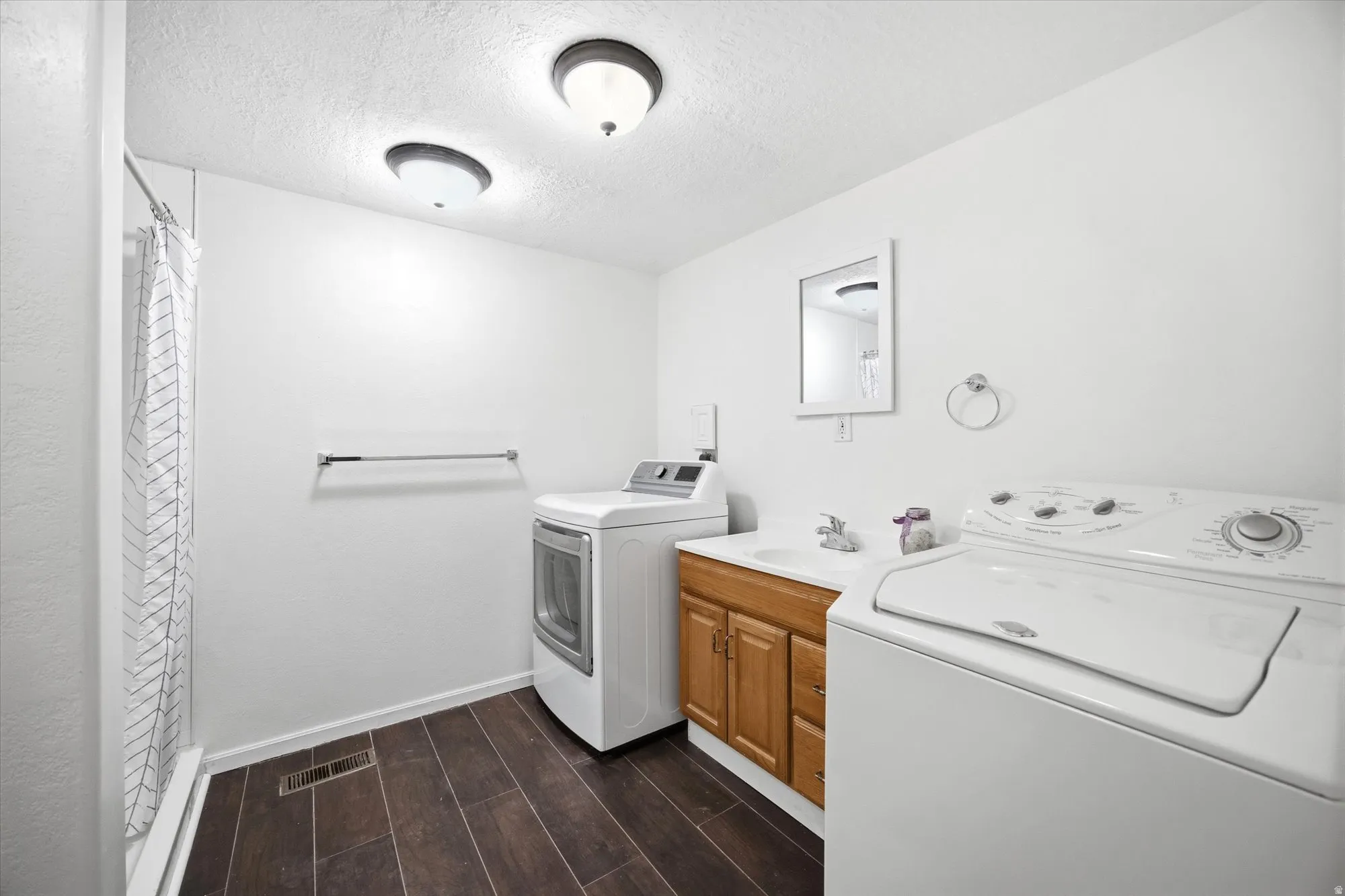 Laundry area with a textured ceiling, wood tiled floors, and washing machine and clothes dryer