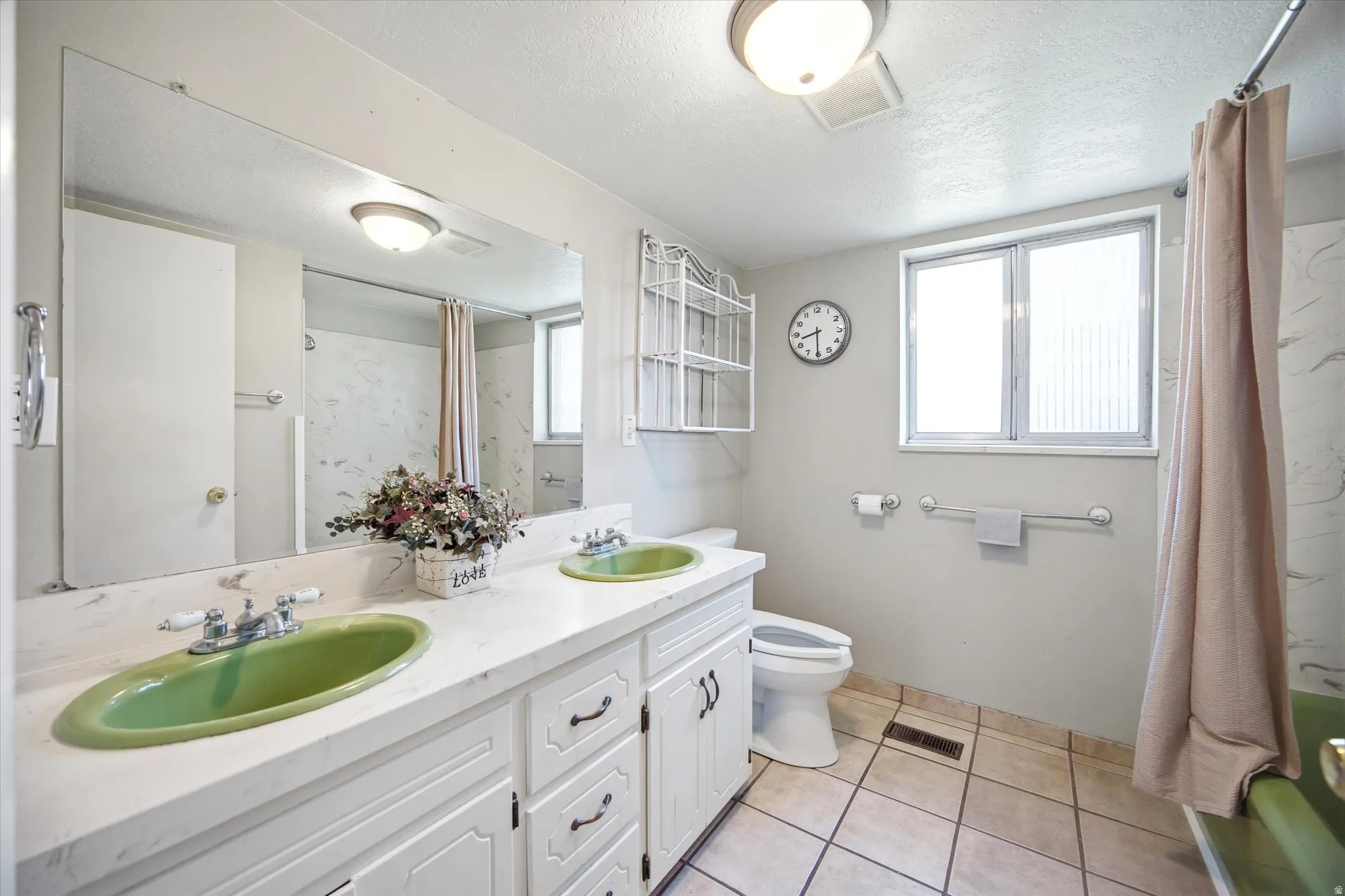 Full bathroom featuring double vanity, shower / bath combo with shower curtain, light tile patterned floors, and a textured ceiling