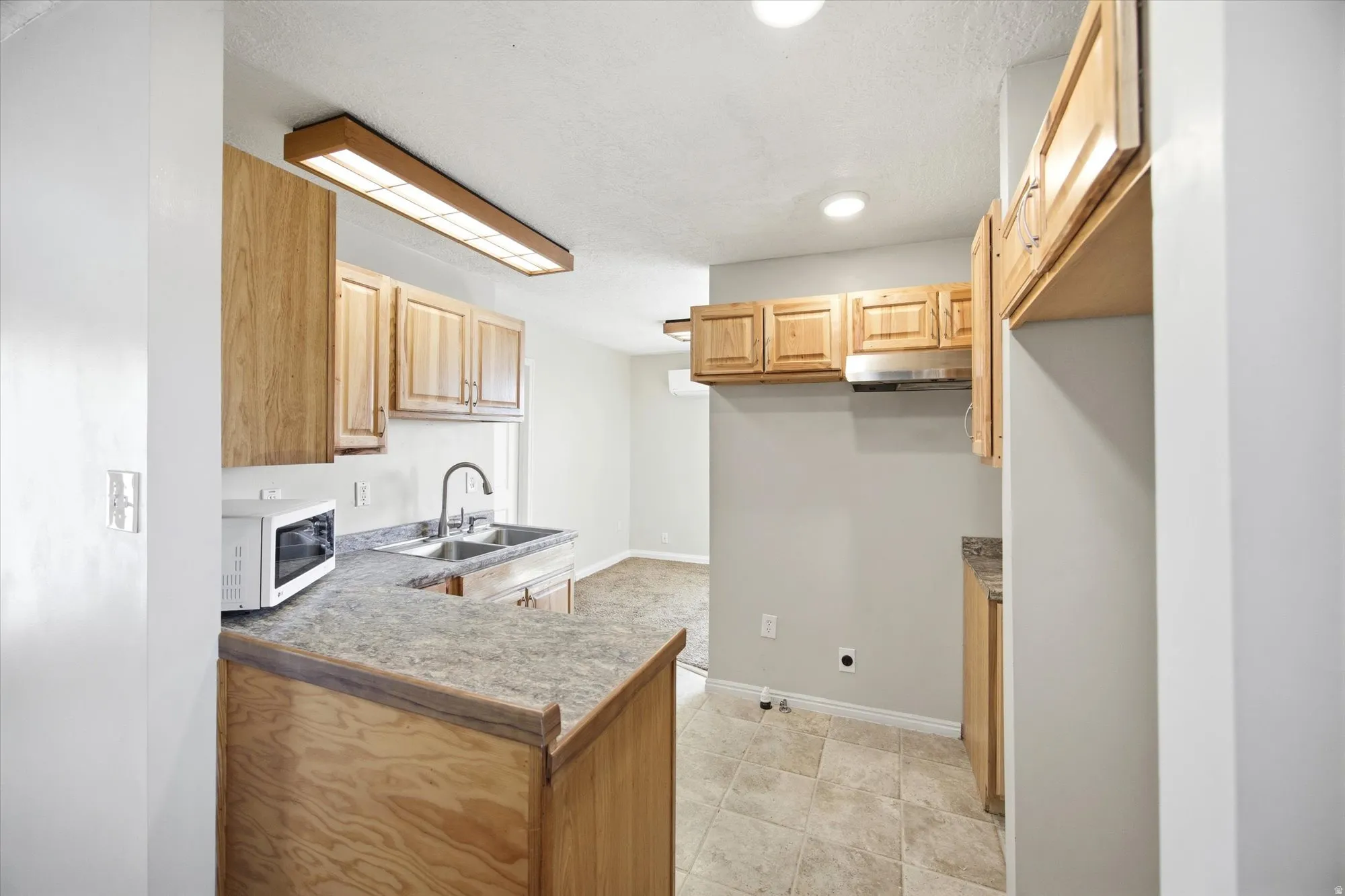 Kitchen featuring white microwave, light wood finish cabinetry, a peninsula, light countertops, and recessed lighting