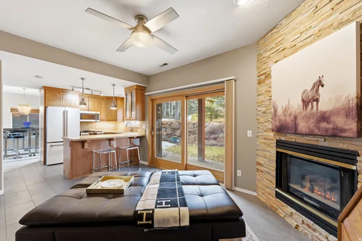 Living room featuring ceiling fan, a stone fireplace, and light tile patterned floors