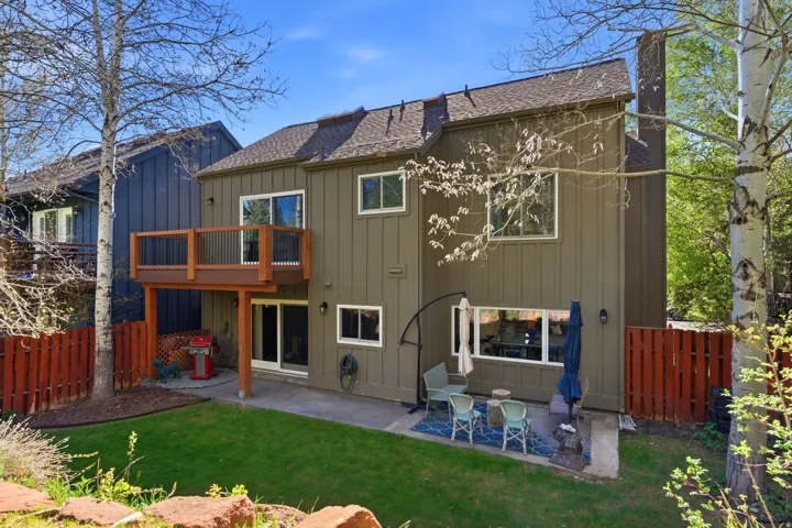 Rear exterior featuring a wood-plank deck, stone patio, sliding glass doors, and a manicured lawn